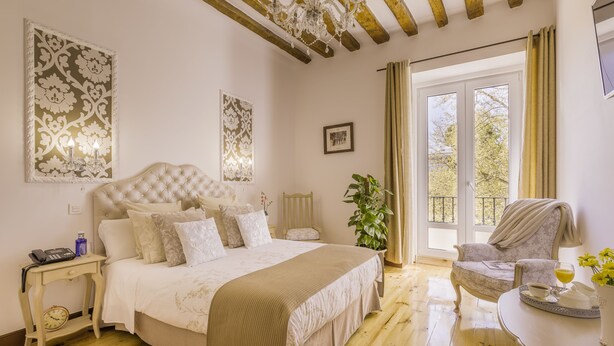 Un dormitorio con una cama grande, una mesita de noche con lámpara, una silla y vistas al exterior a través de una ventana.