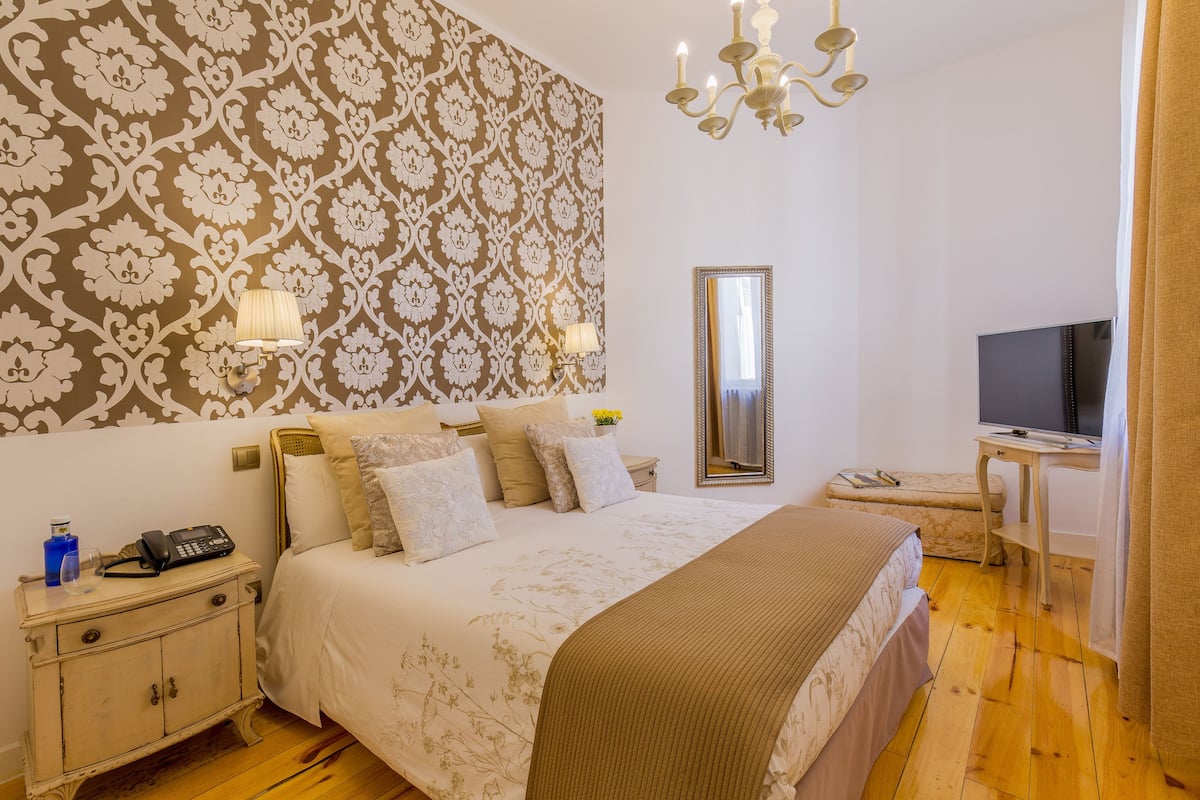 A bedroom with a large bed, bedside lamps, a nightstand, a TV, and a mirror.