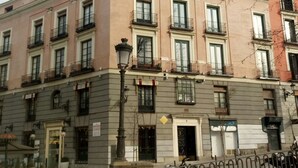 Un edificio de varios pisos con balcones, una farola y una tienda con un letrero.