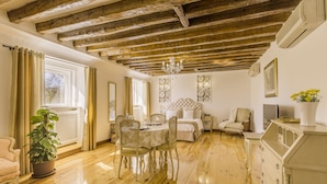 Una habitación con techo de madera, una mesa de comedor con sillas, una cama con cabecera, una silla, una planta en maceta y un aparador.