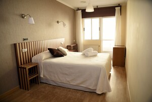 Una habitación de hotel ordenada con una cama grande, mesitas de noche, un radiador y una ventana con cortinas.