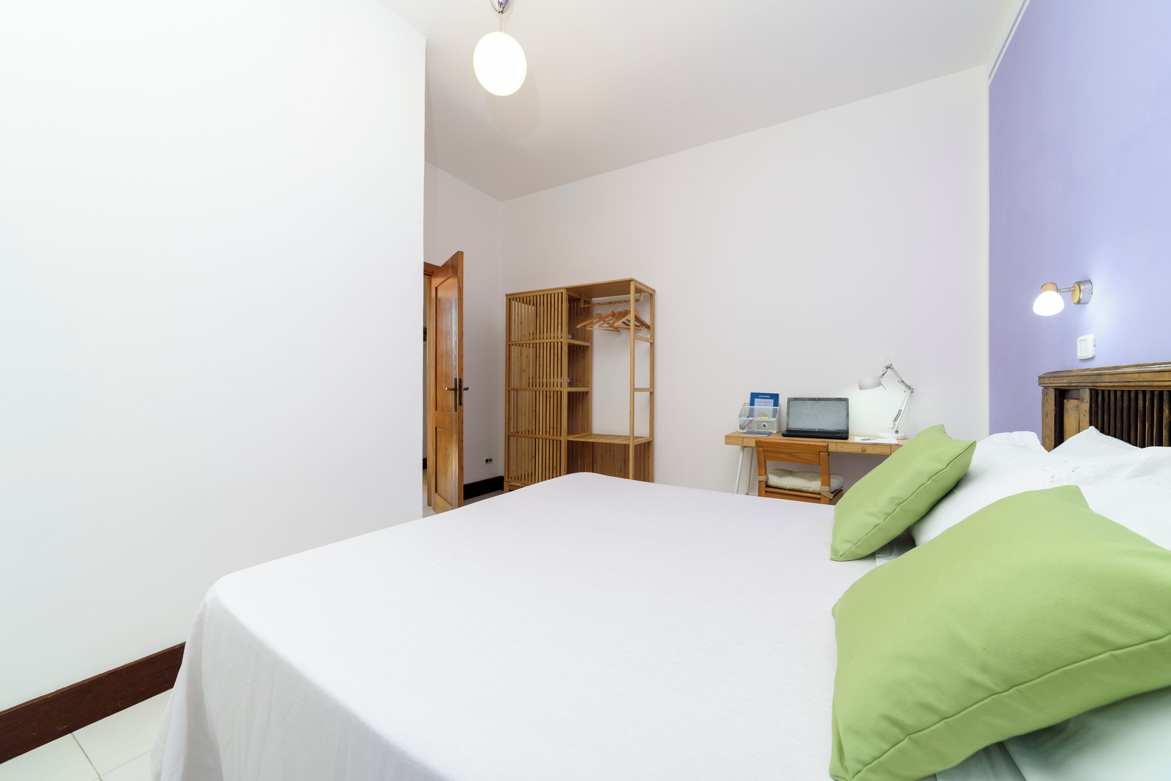 Un dormitorio con una cama, un armario de madera, un escritorio con una computadora y una lámpara.