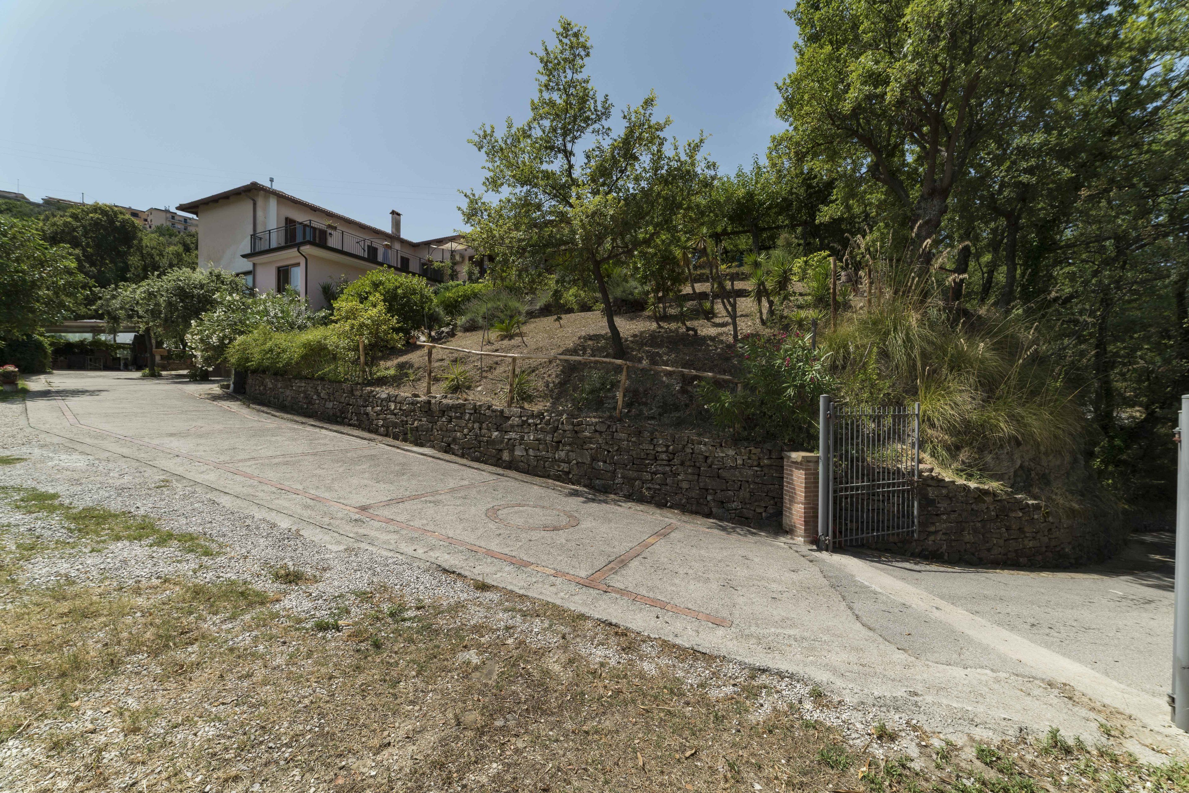 Zona residencial con entrada pavimentada, pared de piedra y acceso porticado.