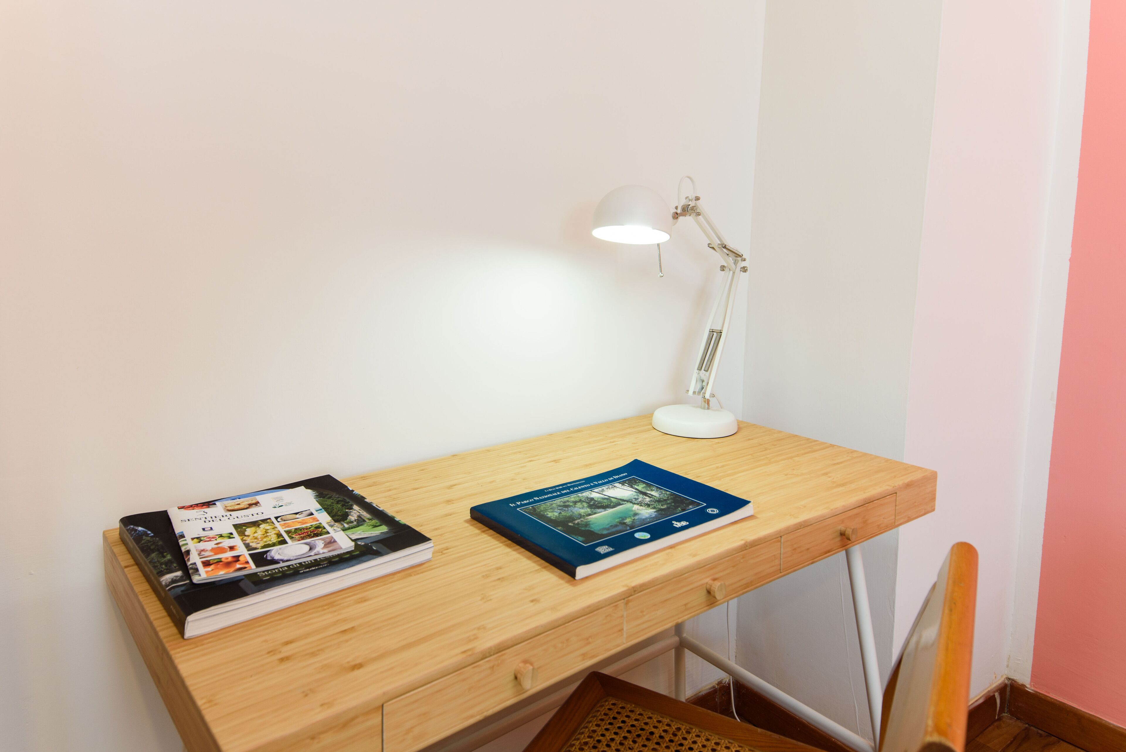 Un escritorio de madera con dos libros y una lámpara de escritorio blanca.