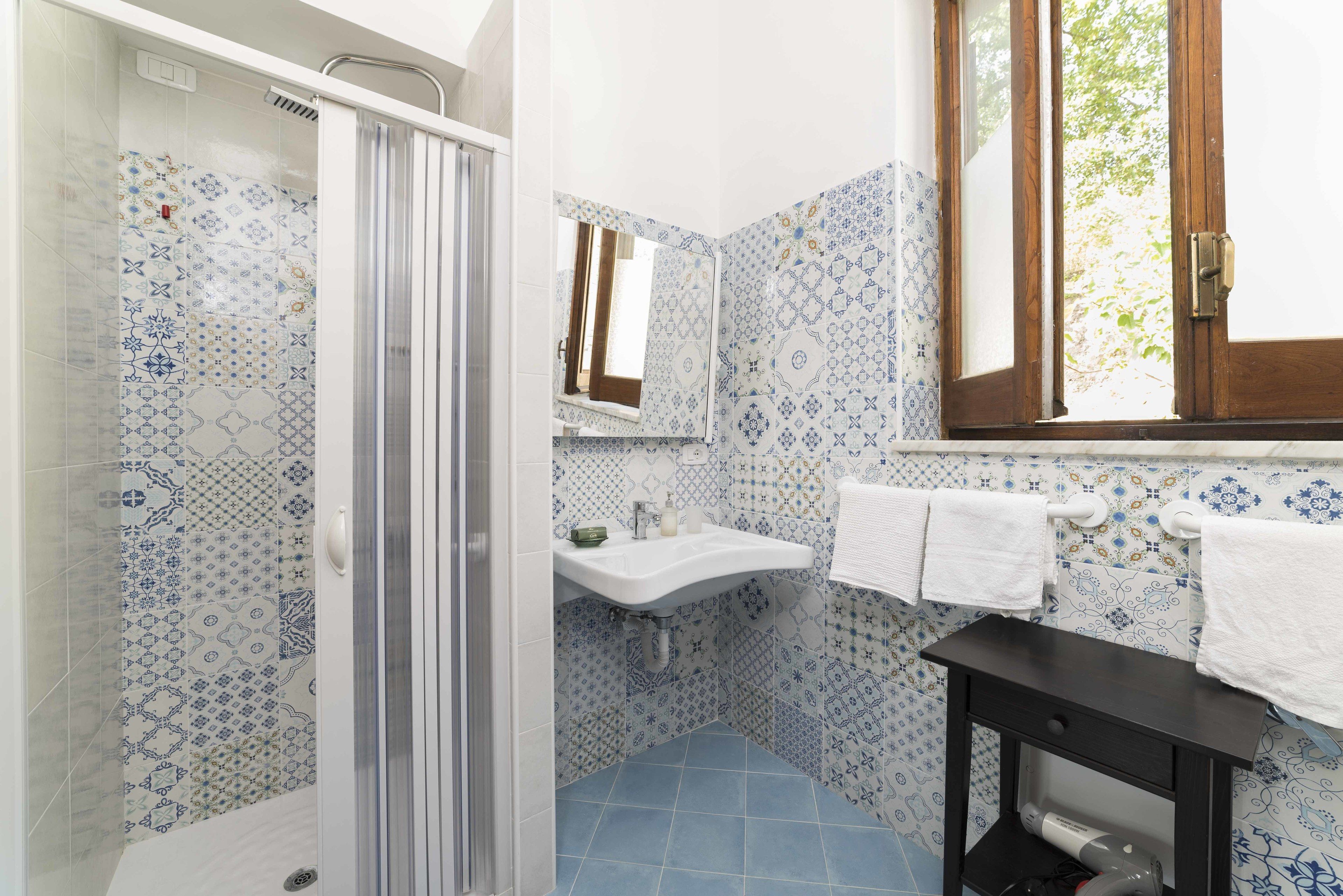 A bathroom with patterned tiles, a sink, a mirror, and a window.