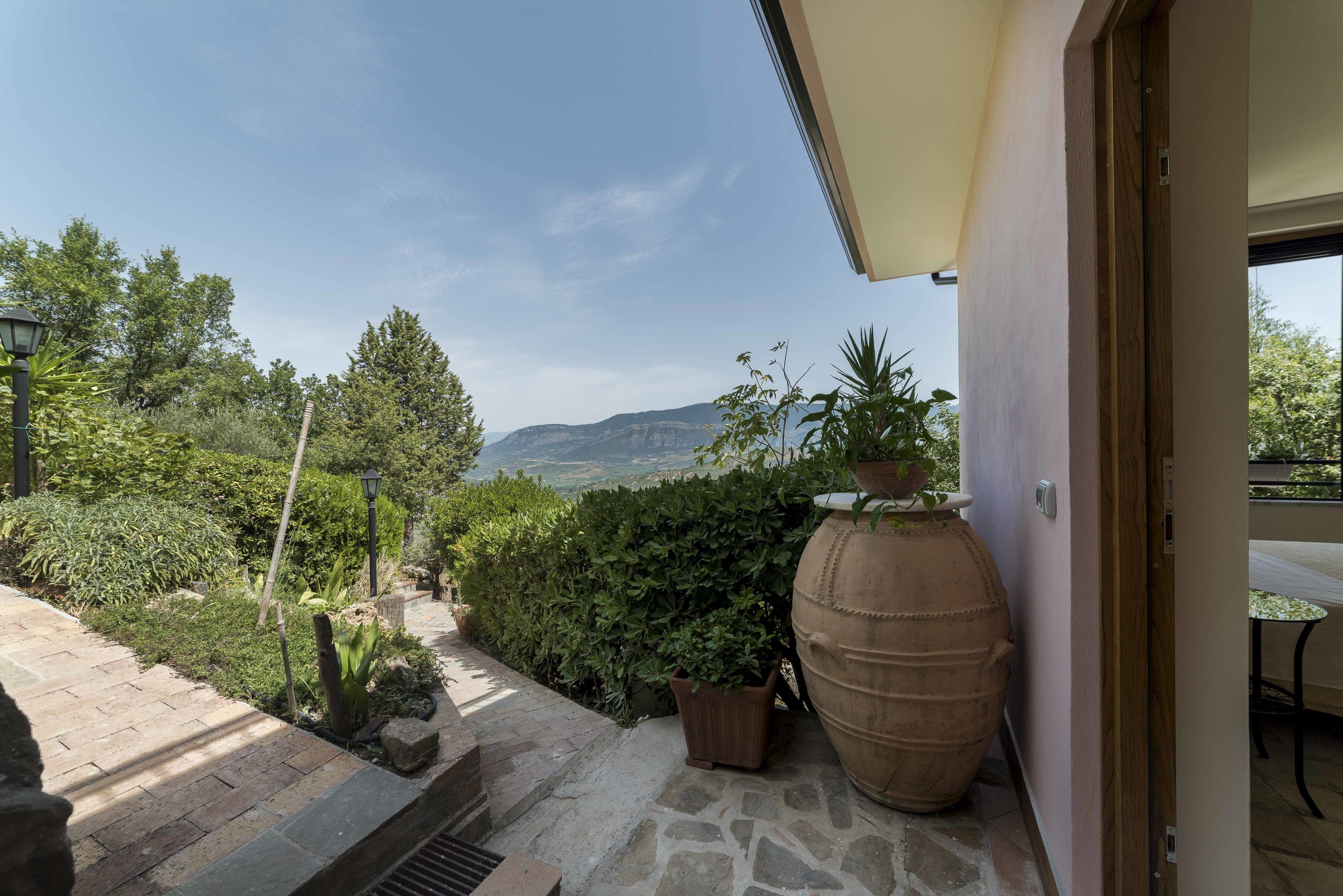 A patio with a stone pathway leading to a door, a large pot, and a view of mountains.