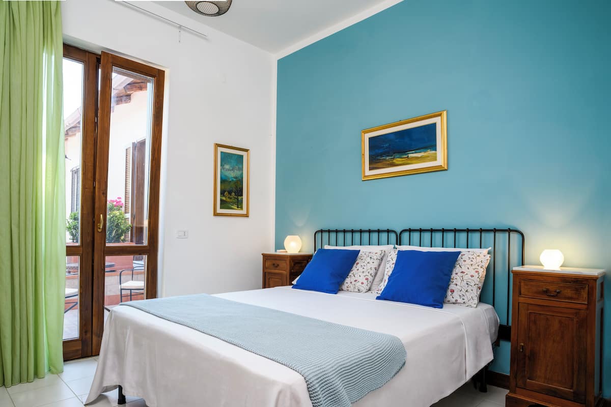 A bedroom with a bed, two bedside tables, a window with curtains, and a painting on the wall.