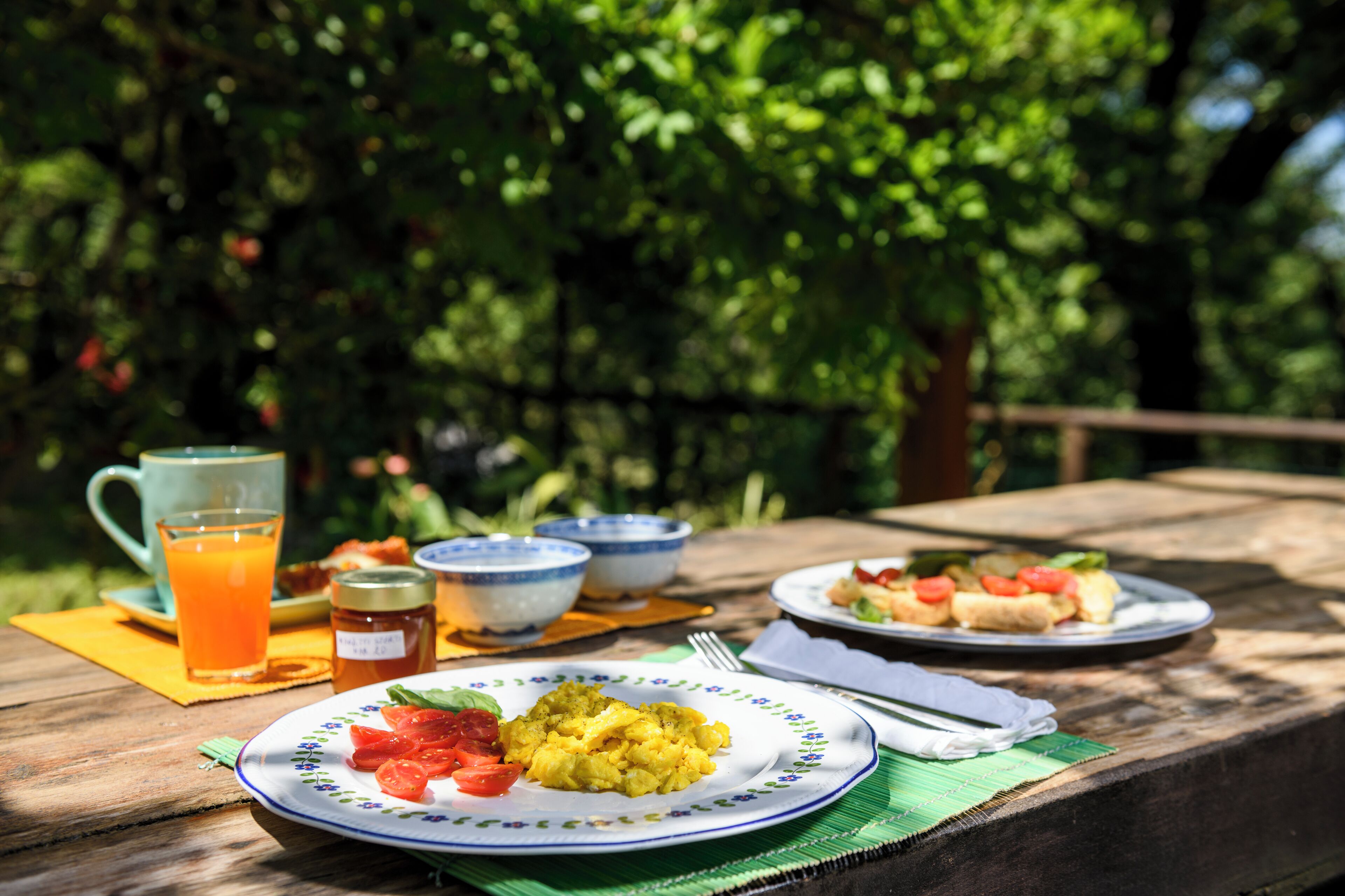 Ein Picknicktisch mit Tellern voller Essen, einem Glas Orangensaft und einem Einmachgläsern.