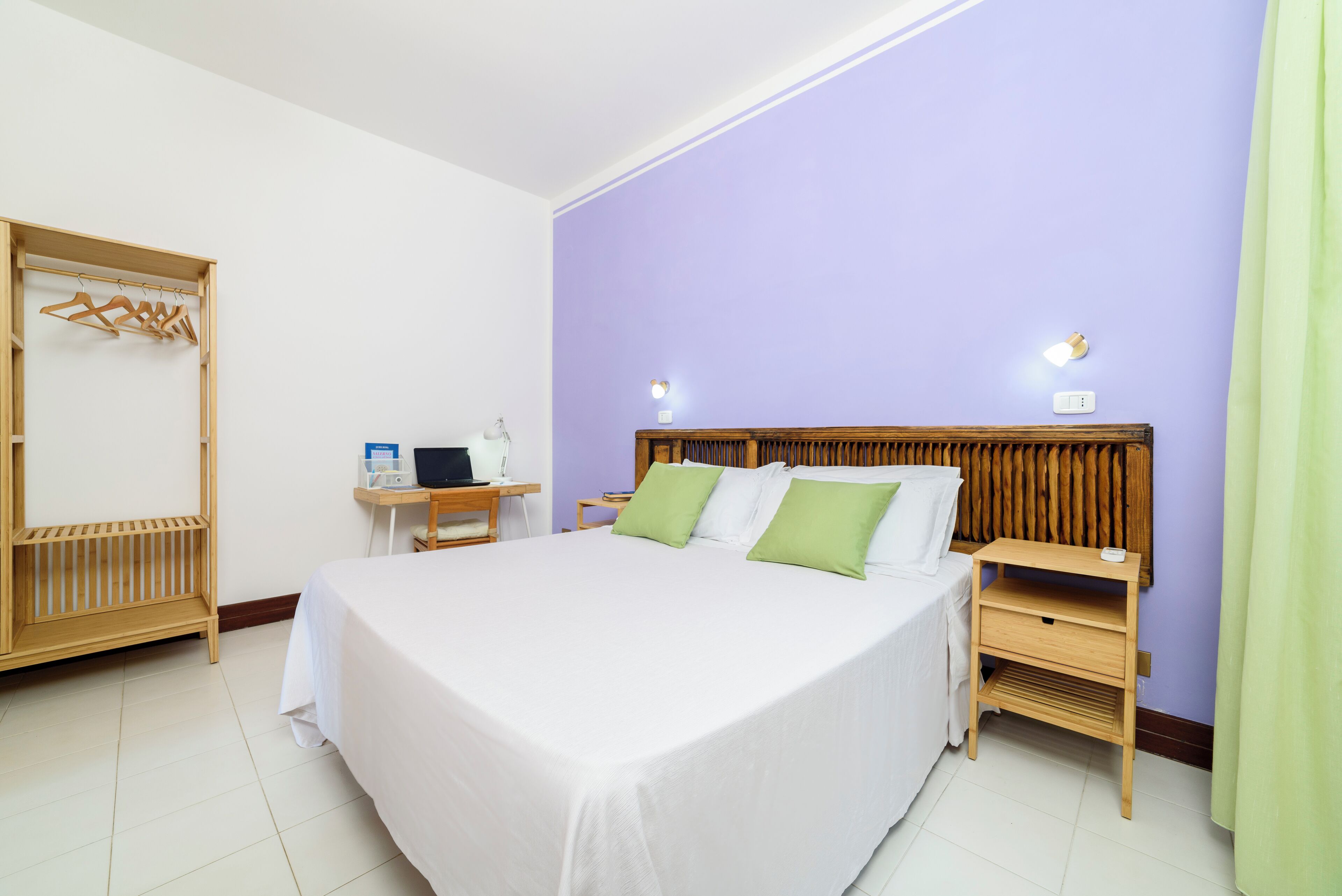 Ein ordentlich eingerichtetes Hotelzimmer mit einem großen Bett, Nachttischen, einem Holzschrank und einem Schreibtisch mit Stuhl.