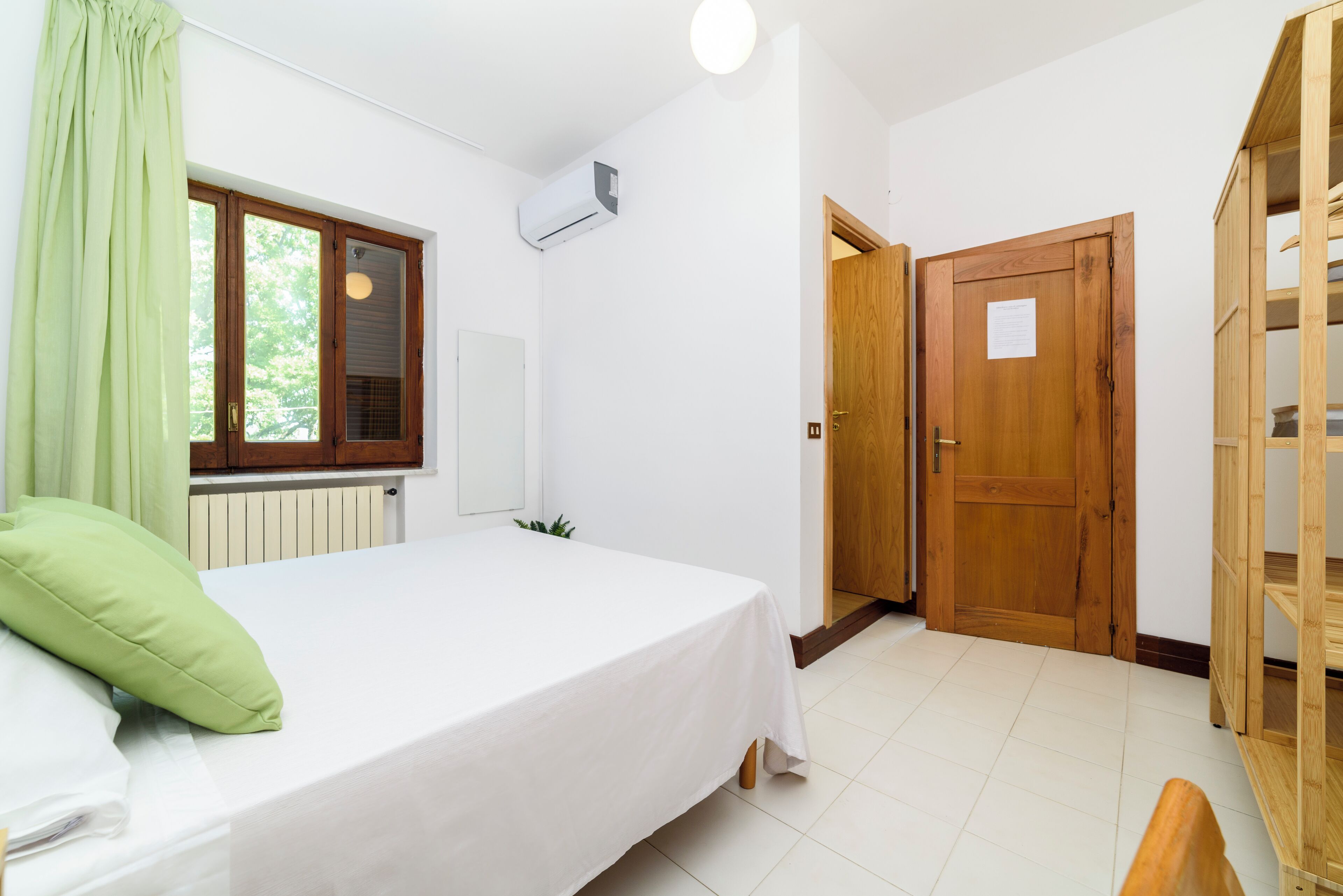 Un dormitorio con cama, ventana con cortinas, aire acondicionado y armario de madera.