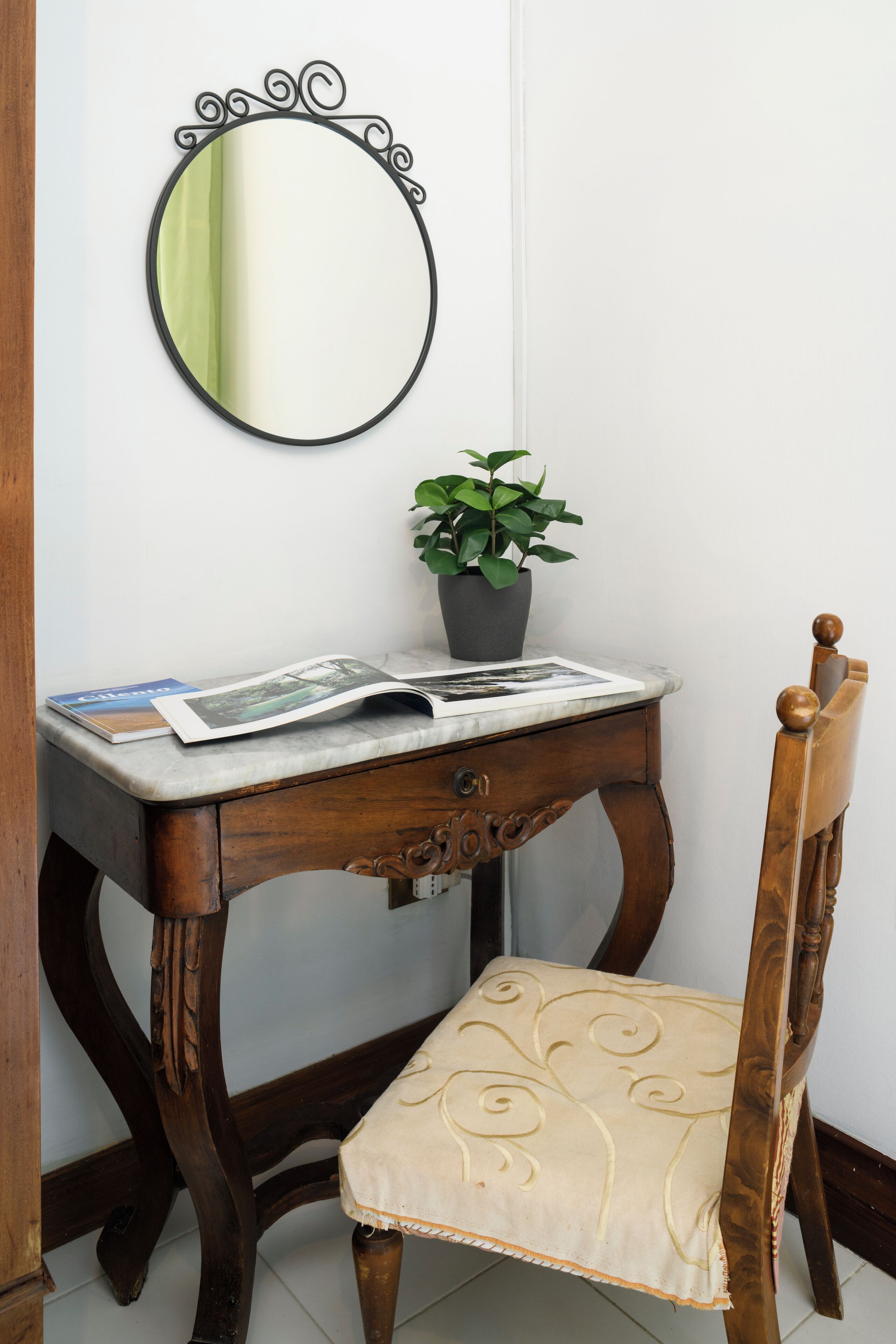 A wooden desk with a mirror, a potted plant, and a chair with a cushion.