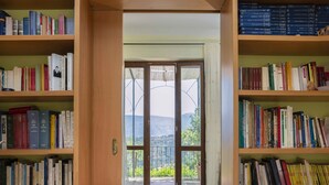 A library with bookshelves on both sides and a view of a mountainous landscape through a glass door. - Albachiara Casa Di Campagna B&B (Ogliastro Cilento)