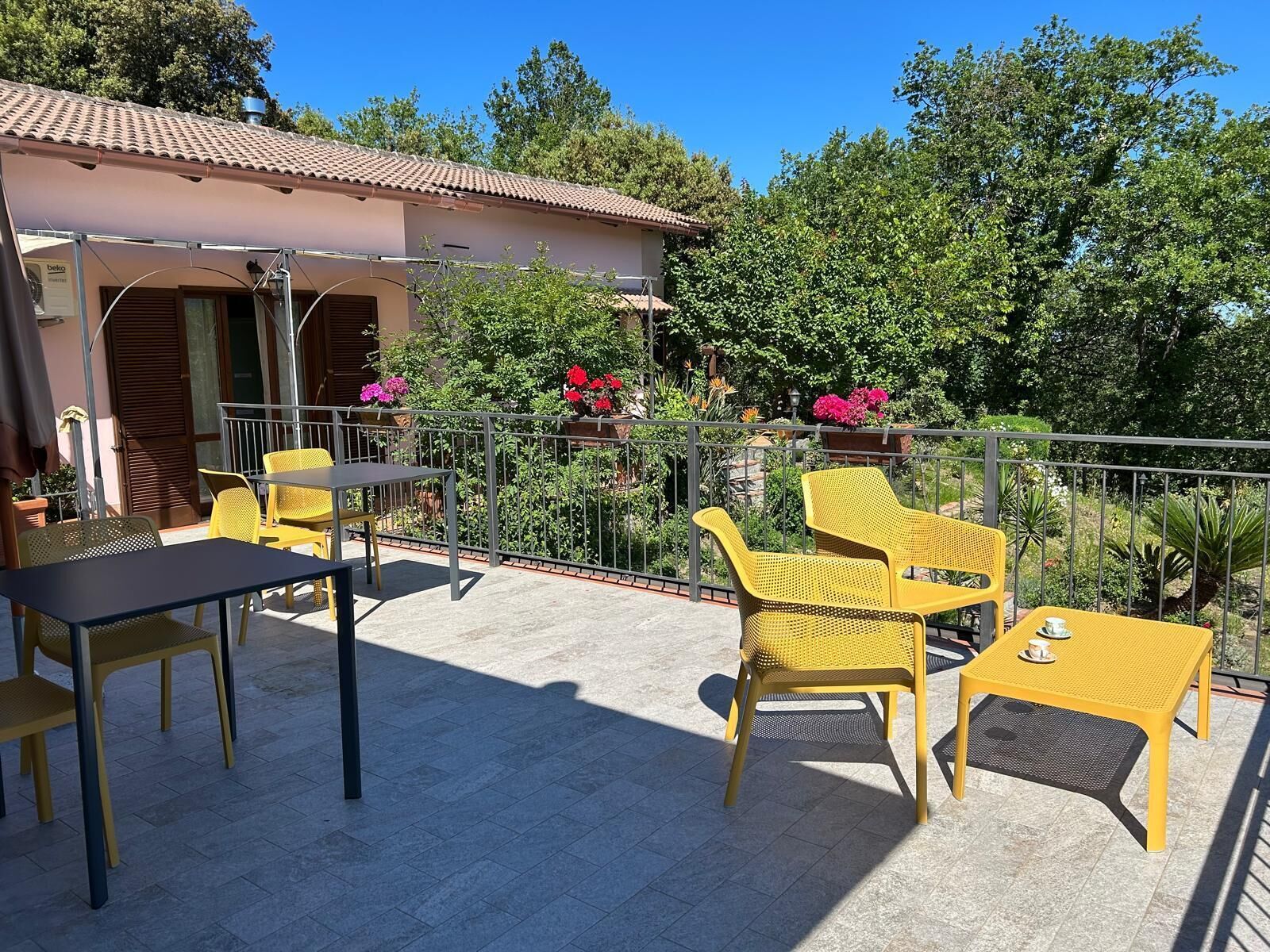 Eine Terrasse mit gelben Stühlen und einem Tisch, umgeben von einem Metallgeländer und Blumentöpfen.