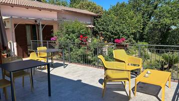 Eine Terrasse mit gelben Stühlen und einem Tisch, umgeben von einem Metallgeländer und Blumentöpfen.