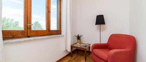 A room with a wooden floor, a red armchair, a small table with a plant, and a floor lamp.