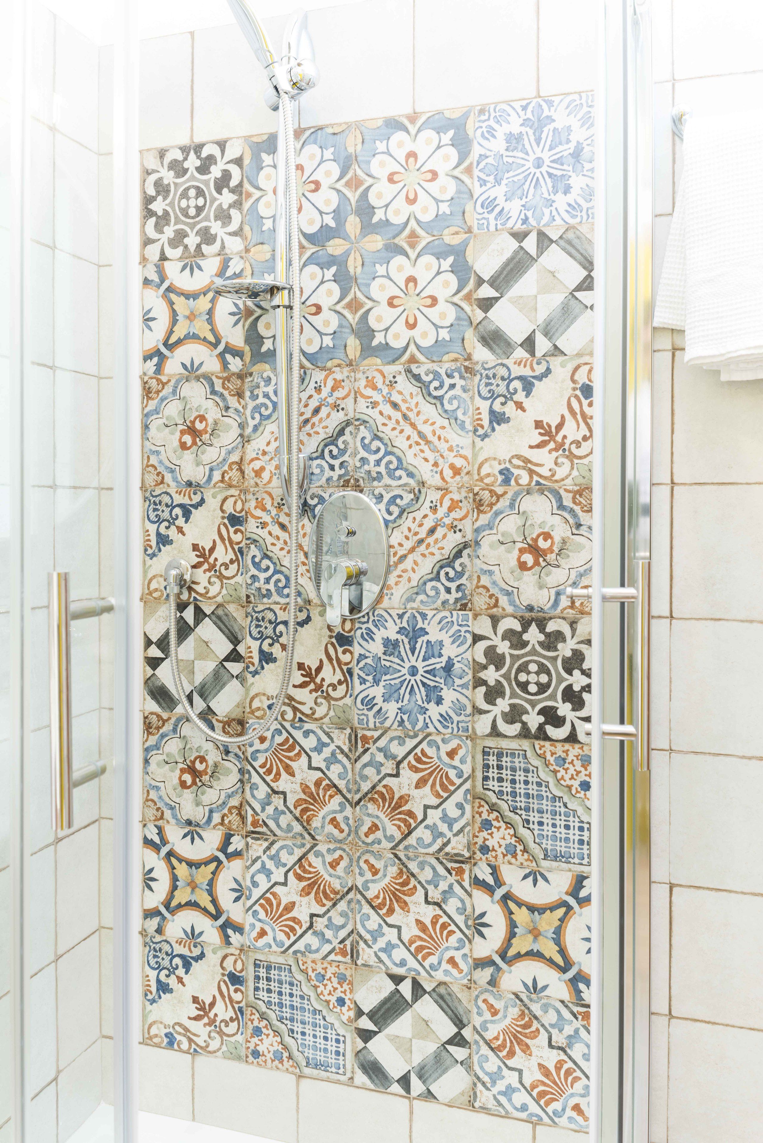 Ein Duschbereich mit Glastür und gefliesten Wänden, die verschiedene geometrische und florale Muster zeigen.