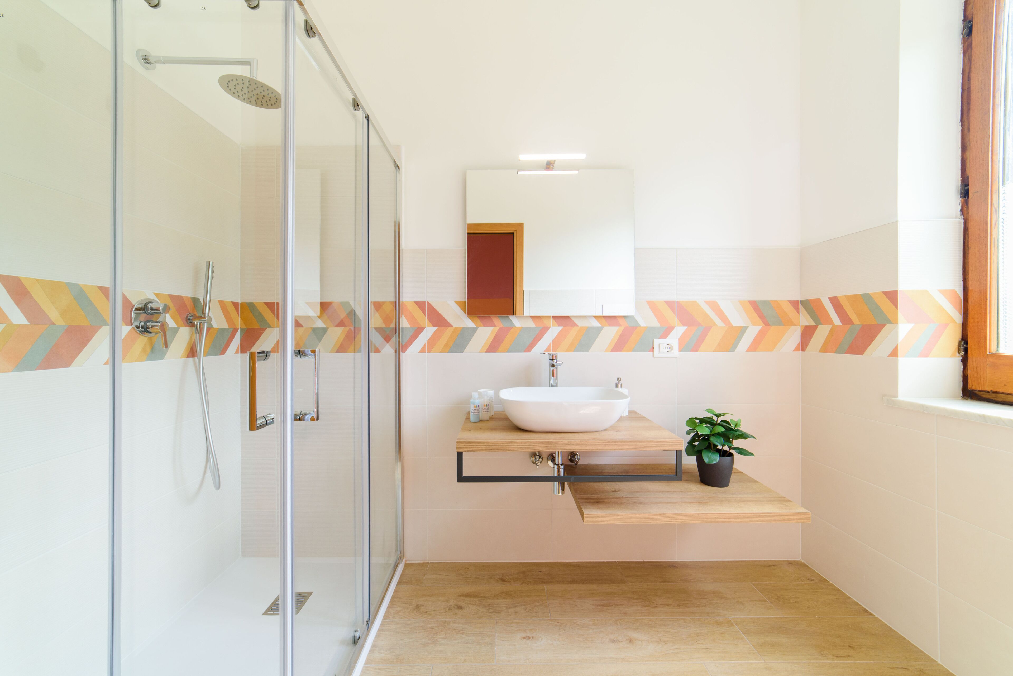 A modern bathroom with a glass shower enclosure, a wooden vanity with a white sink, and a chevron-patterned backsplash.