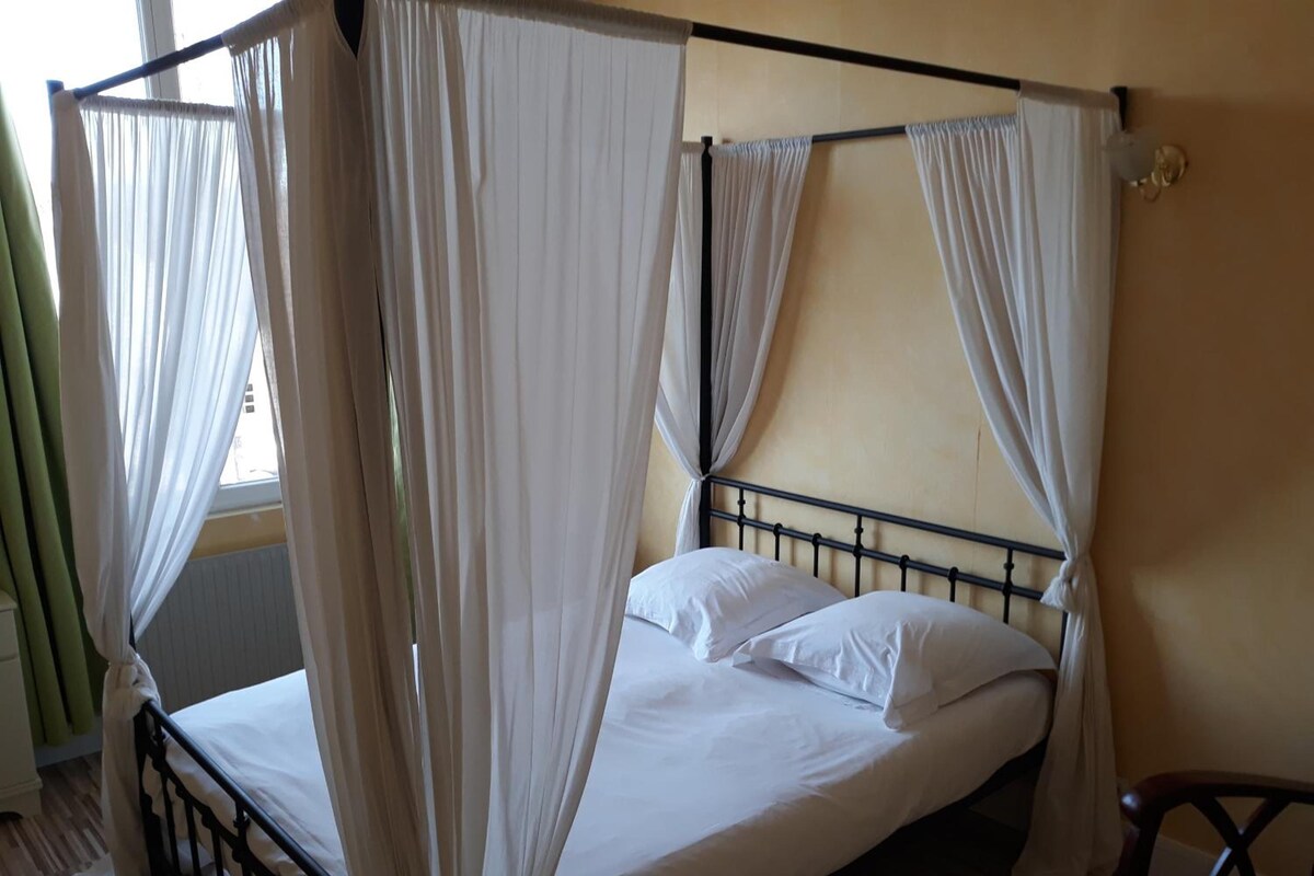 Una cama individual con estructura metálica, ropa de cama blanca y un dosel con cortinas traslúcidas.