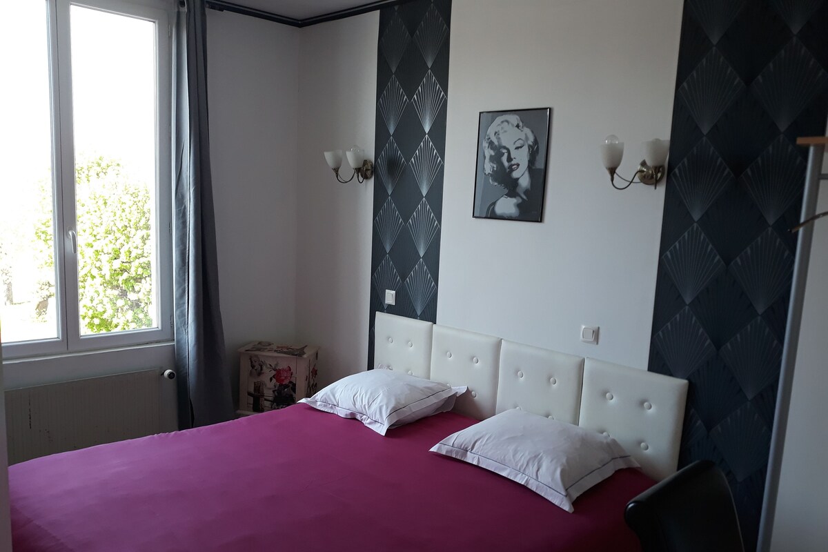 A bedroom with a bed, two wall sconces, a framed picture, and a window.