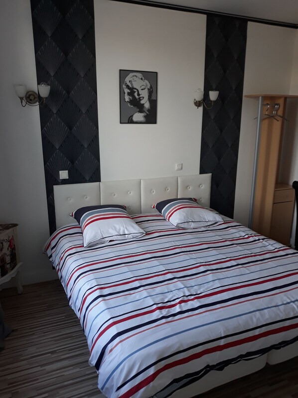 Una cama con ropa de cama a rayas, un cabecero y un cuadro colgado en la pared.