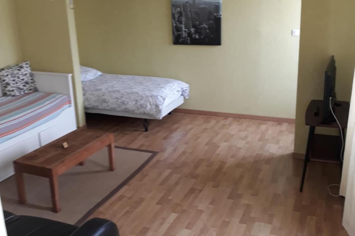 A small, furnished room with a bed, a sofa, a wooden bench, and a television on a stand.
