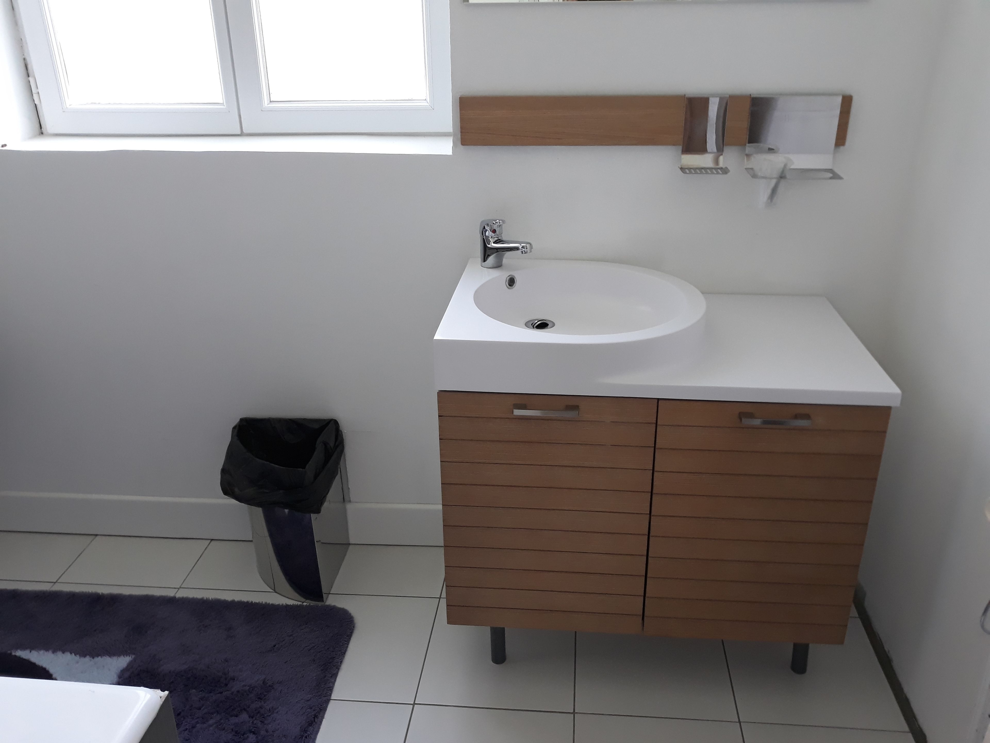 Un baño con un lavamanos blanco, un armario de madera y un pequeño cubo de basura.