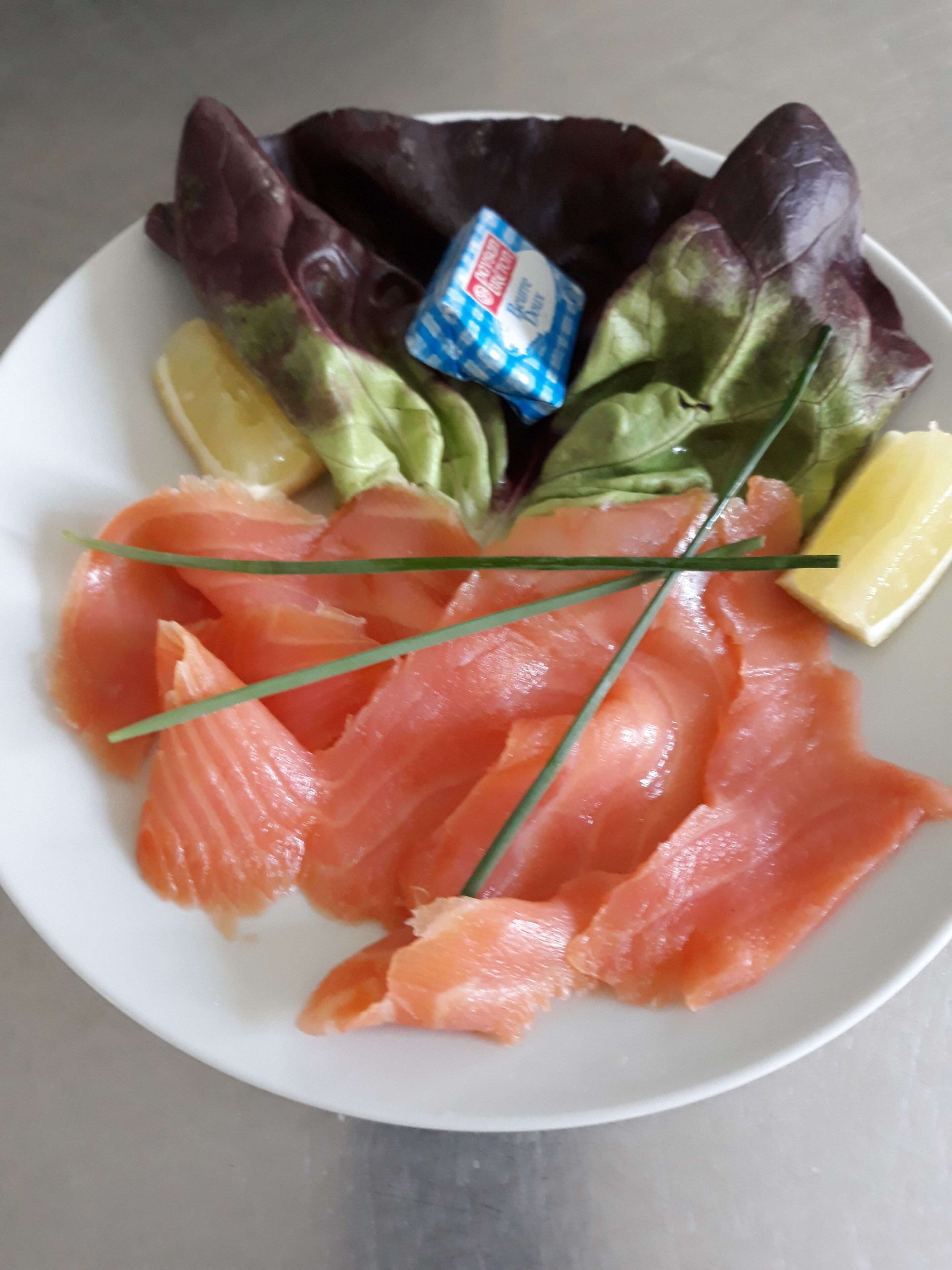 Ein Teller mit Lachs, Salat und einer Zitronenscheibe.