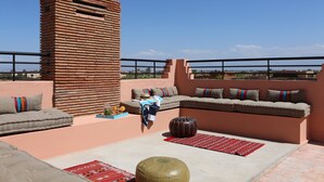 A rooftop terrace with a brick structure, a cushioned seating area, and a view of the landscape. - Villa Zahoua (Marrakech)