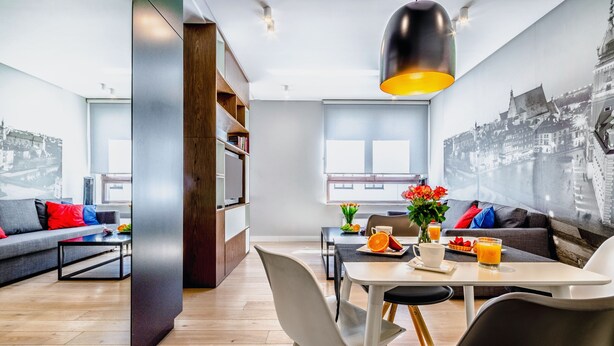 A modern living room with a dining area, featuring a cityscape mural, a dining table with chairs, and a sofa with colorful cushions. - Business Center Phoenix Apartments (Warsaw)