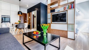 A modern living room with a black coffee table, a sofa, and a TV on a wooden shelf. - Business Center Phoenix Apartments (Warsaw)