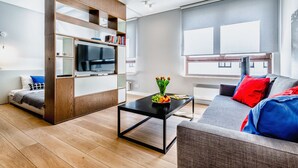 A modern living room with a sofa, a coffee table, a TV, and a bookshelf. - Business Center Phoenix Apartments (Warsaw)