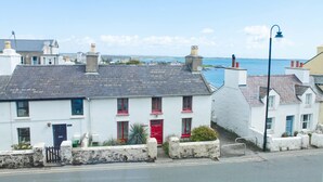 A coastal building with a red door, white walls, and a stone wall in front. - Carrick Rooms (Port St Mary)