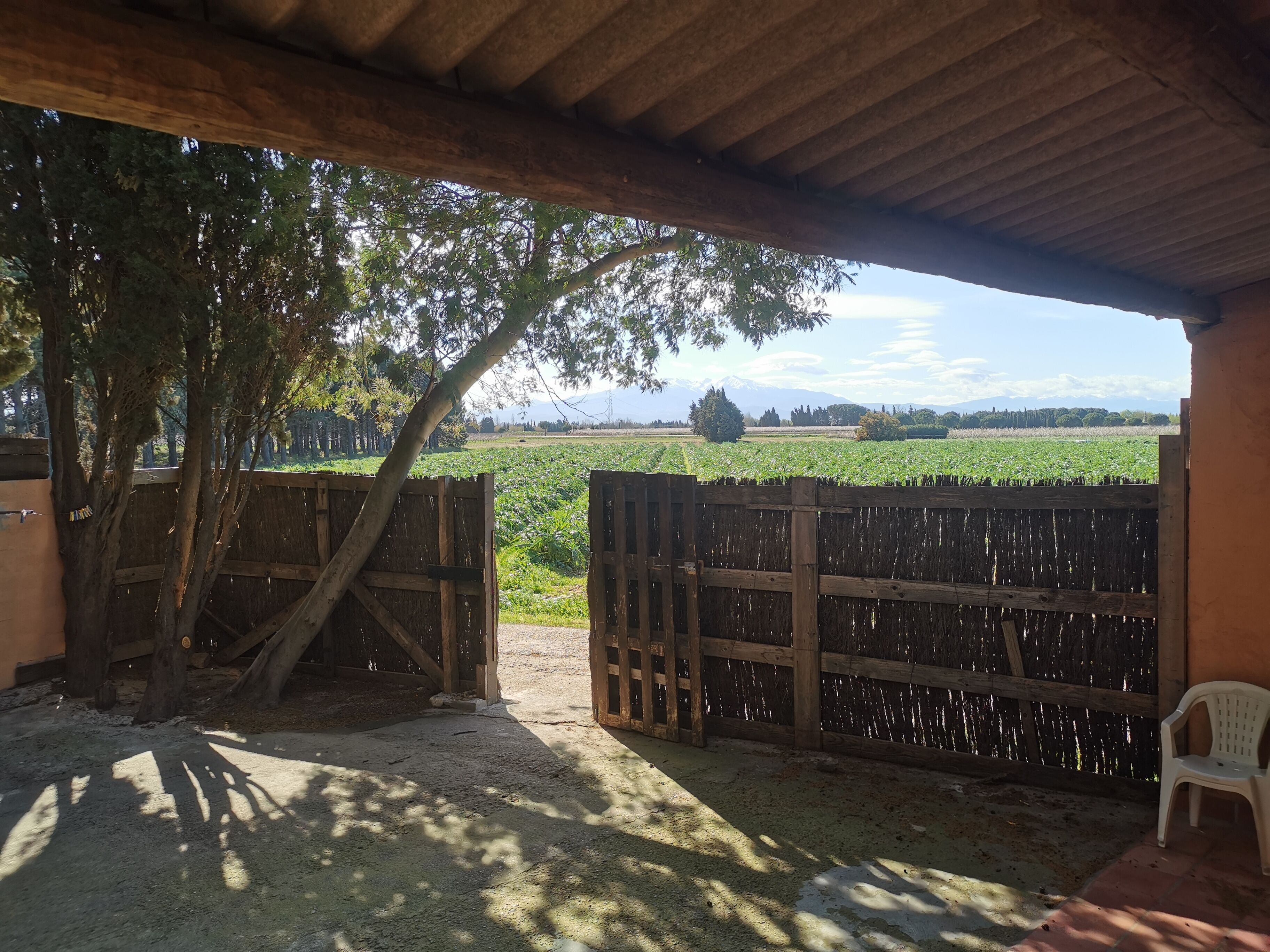 A covered outdoor area with a wooden fence, a chair, and a view of a field and mountains in the background.