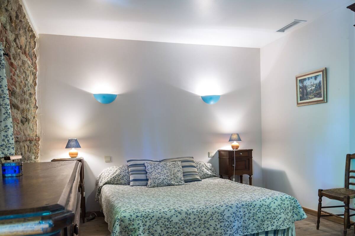A bedroom with a bed, two bedside lamps, a nightstand, a chair, and a painting on the wall.