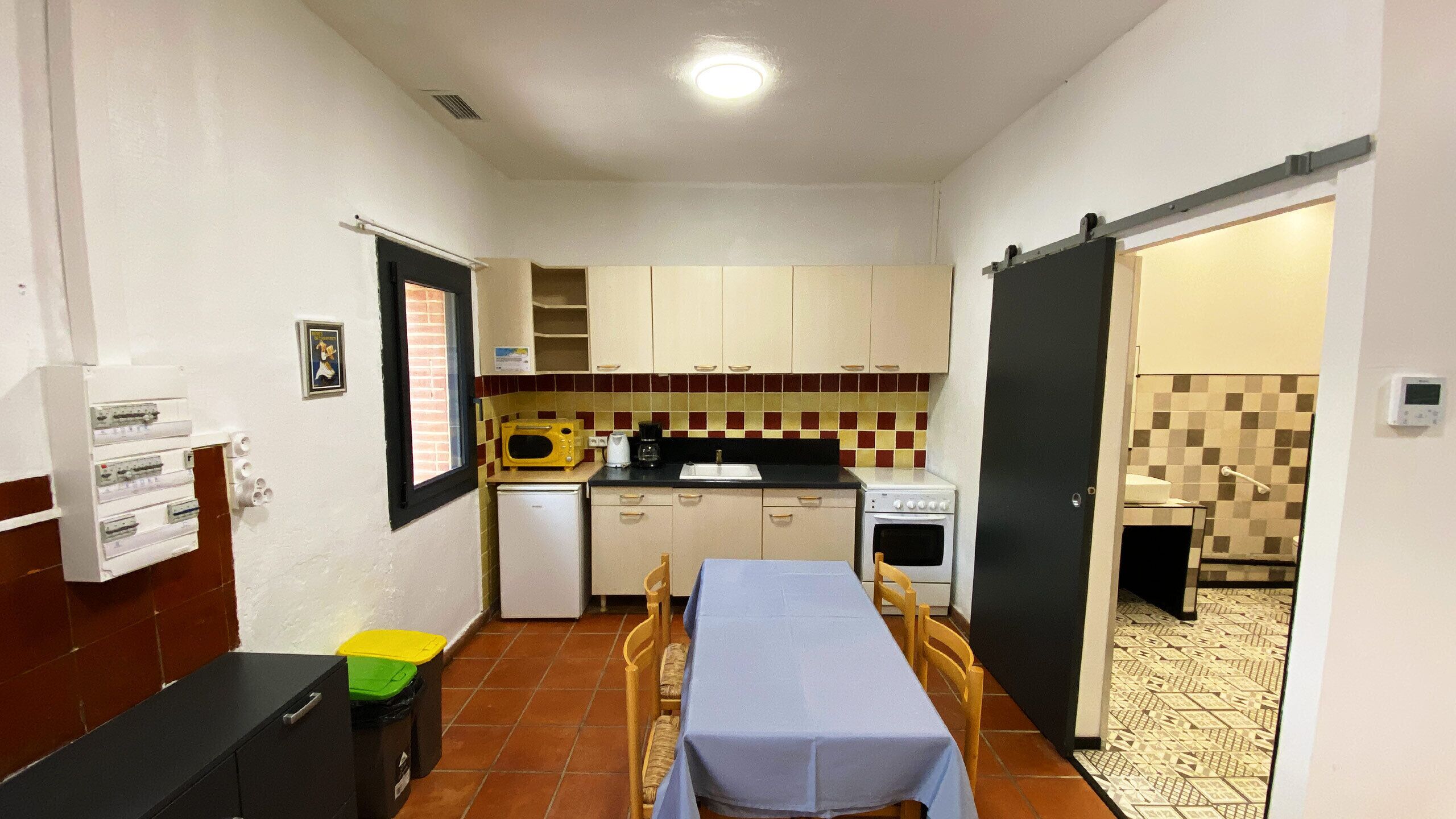 Una cocina compacta equipada con microondas, estufa y lavaplatos. Hay una mesa de comedor con sillas. La cocina tiene un salpicadero de azulejos y una ventana.