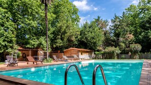 Una piscina amb aigua cristal·lina blava, envoltada d'arbres i un pont de fusta amb gandules.