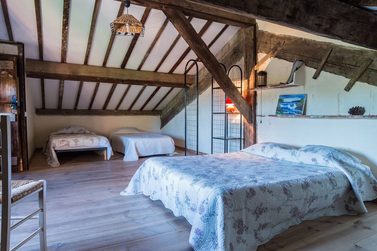 A rustic bedroom with a wooden ceiling, two single beds, a chair, and a painting on the wall.
