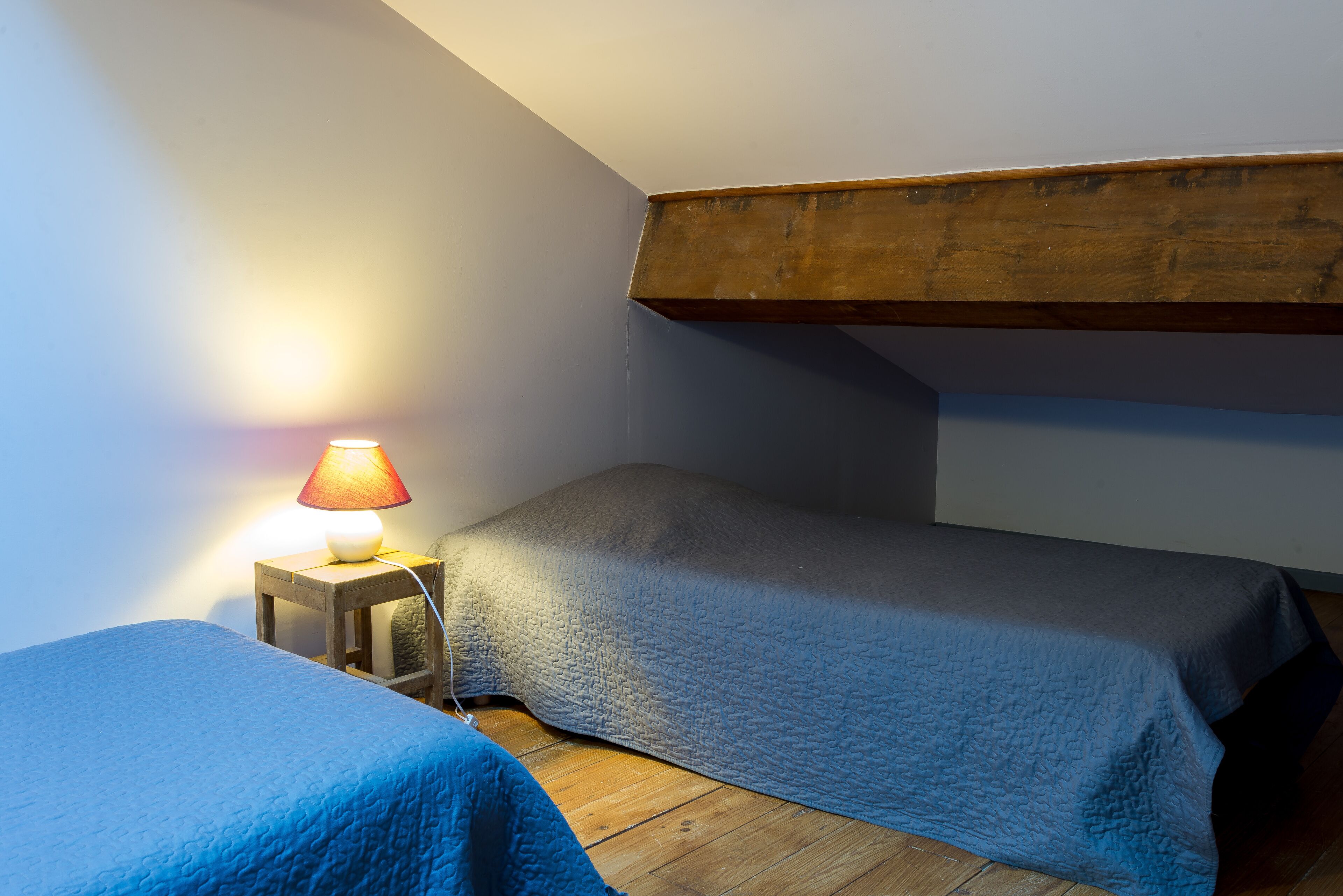Une petite chambre agréable, dotée de deux lits simples, d’une tête de lit en bois, d’une table de chevet avec une lampe et d’un plancher en bois.
