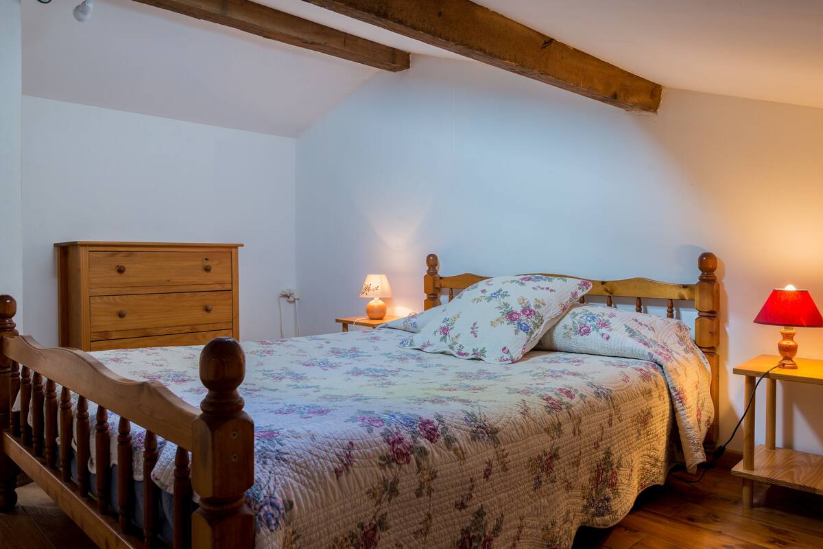 A bedroom with a wooden bed, a nightstand with a lamp, and a wooden dresser.