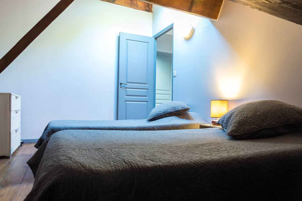 A bedroom with two beds, a wooden ceiling, a white wardrobe, and a nightstand with a lamp.