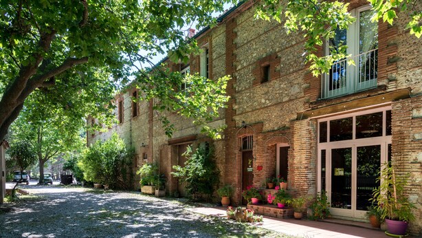 Un pati amb un camí de grava, envoltat d'edificis de maó amb balcons i plantes en testos.