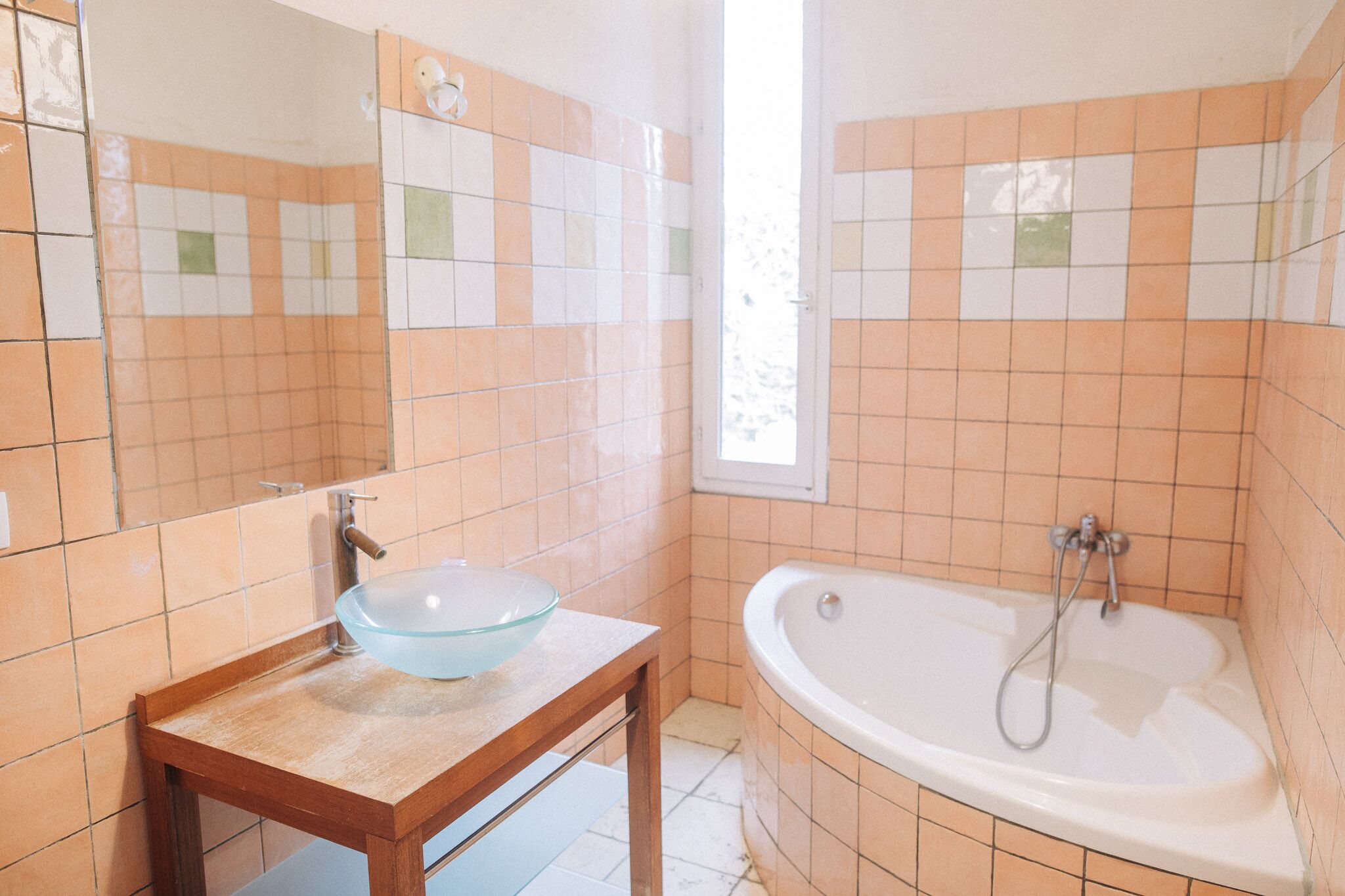 Un baño con un lavabo de vidrio, un mueble de tocador de madera y una bañera blanca.