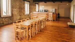 Zona de dinar rústica amb una taula de fusta llarga i caires, una cuina al fons i parets de pedra.