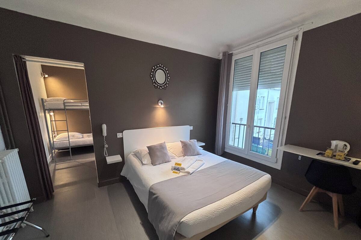 A hotel room with a bunk bed, a desk, and a large window.