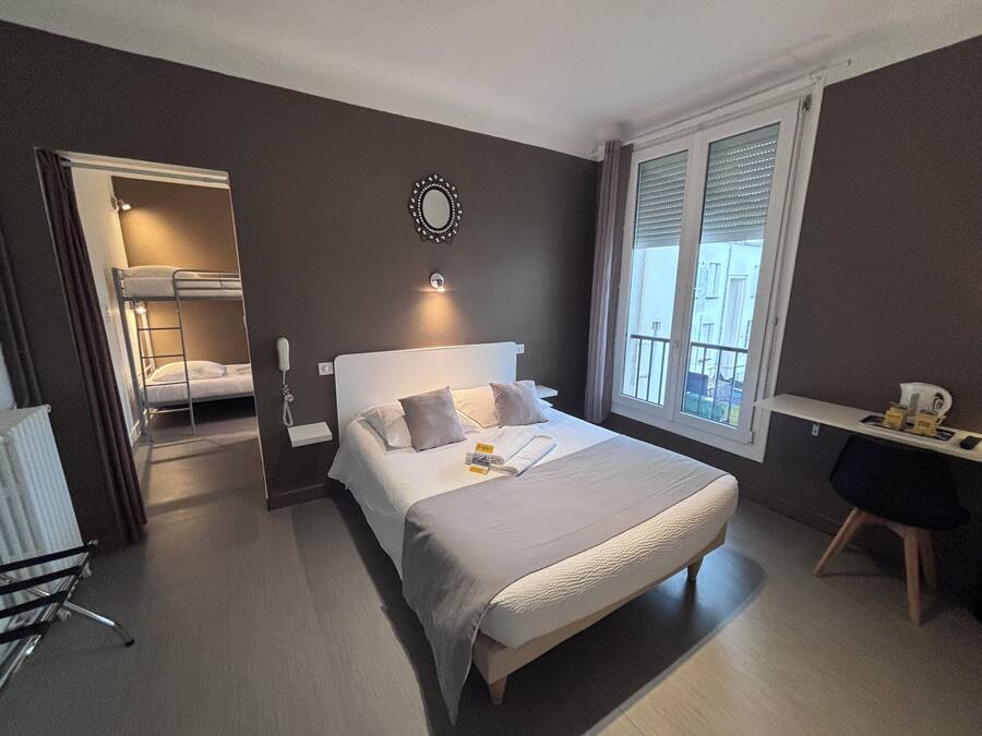 A hotel room with a bunk bed, a desk, and a large window.