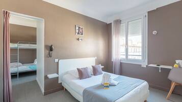 Habitación de hotel con una cama individual, una mesita de noche, una silla, un ventanal con persianas, un teléfono y una puerta que da a un balcón.