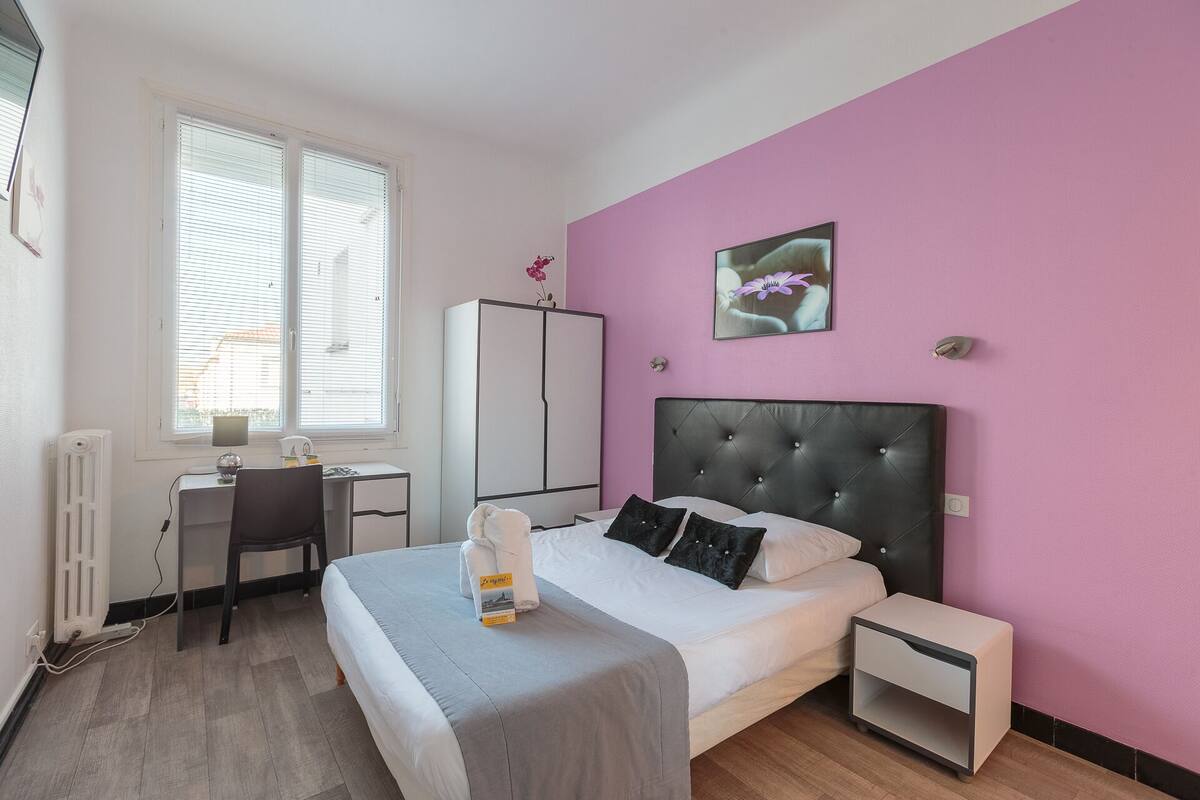 A bedroom with a bed, bedside tables, a desk, and a radiator.
