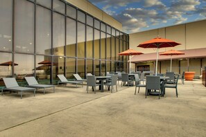 An outdoor seating area with tables and chairs, umbrellas, and a building with large windows in the background. - Mount Vernon Hotel and Event Center (Mount Vernon)