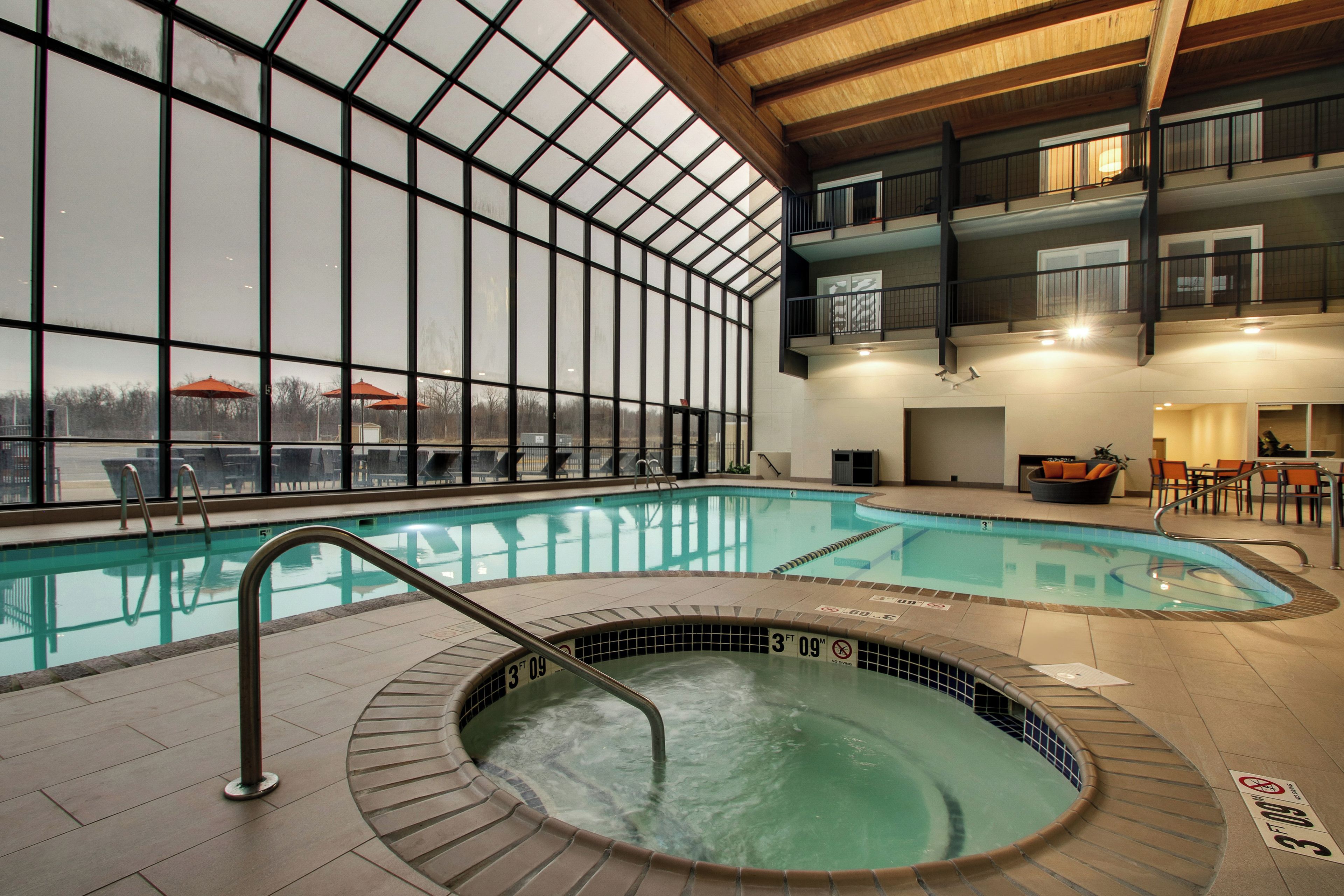 An indoor swimming pool with a hot tub, large windows, and a view of the outside.