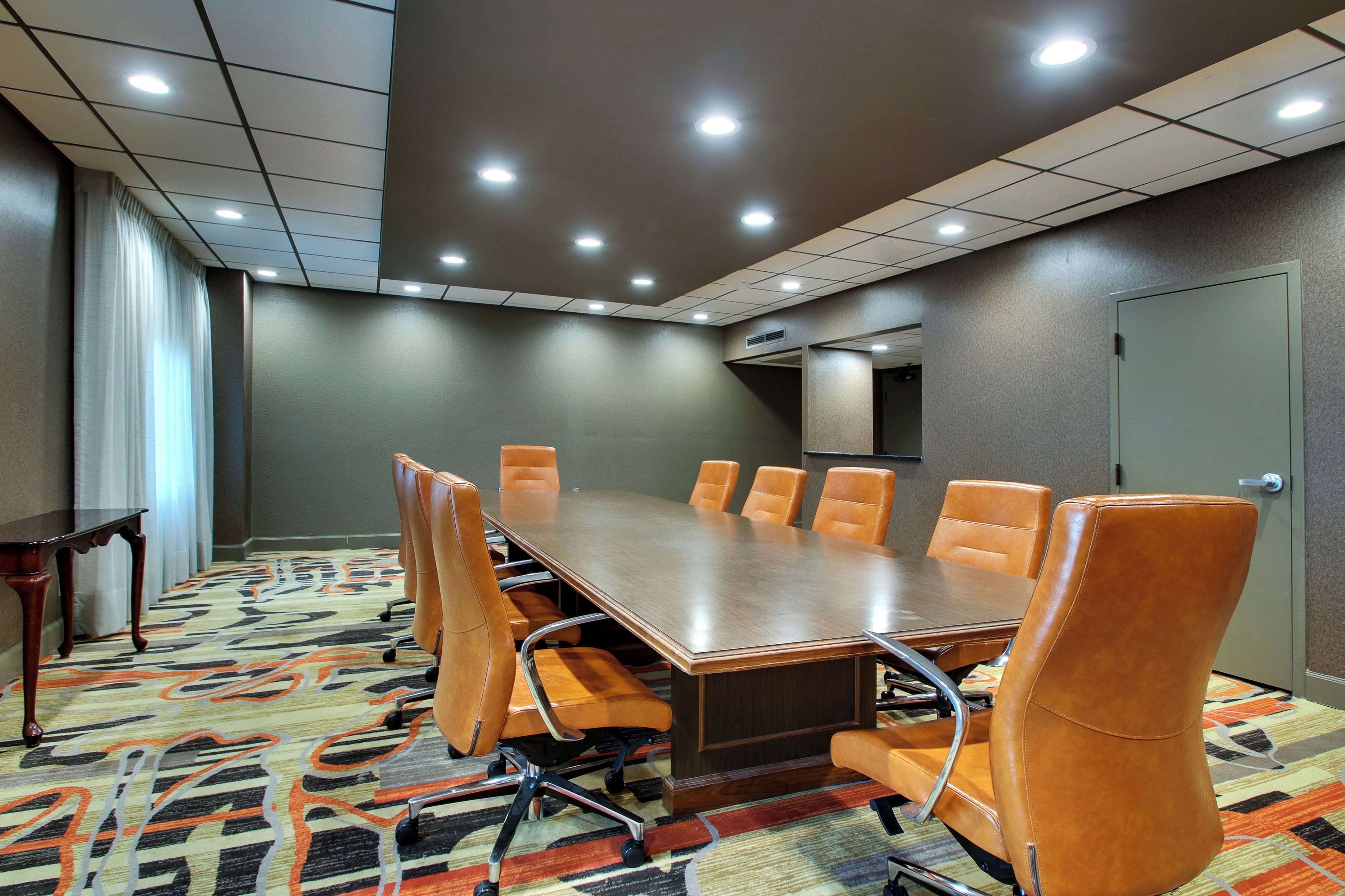 Un salón de conferencias con una mesa larga y ocho sillas, piso alfombrado e iluminación en el techo.